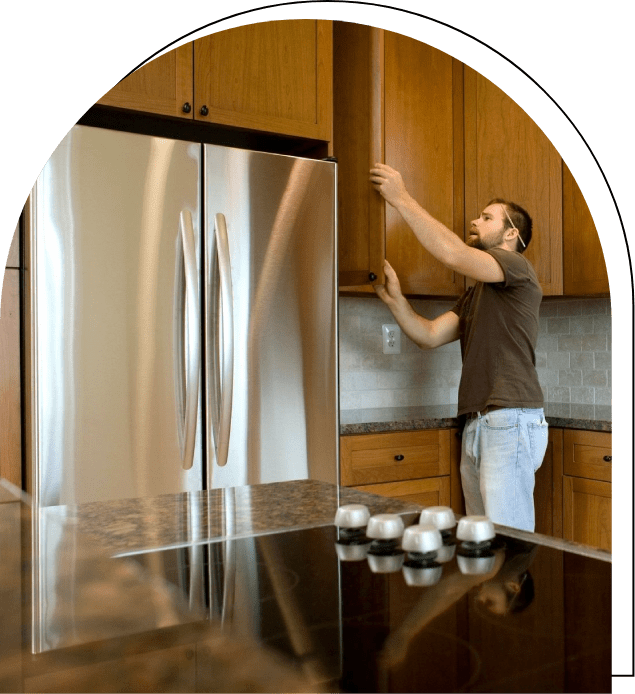 A man in brown shirt and white pants standing next to kitchen counter.