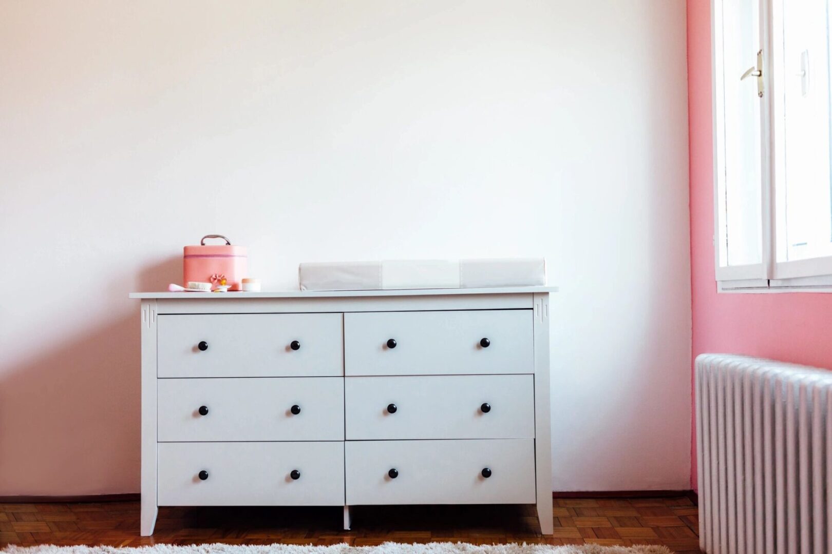 A white dresser with six drawers and a pink teapot on top of it.